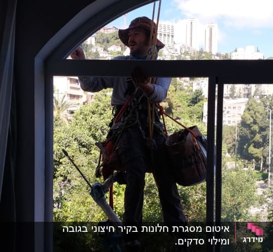 אדם עם ציוד טיפוס מנקה חלון מבחוץ